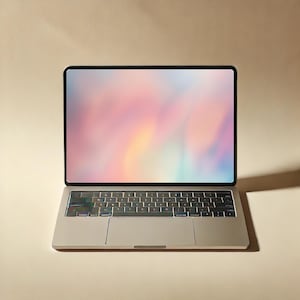 May include: A silver laptop computer with a black screen border. The screen displays a colorful, abstract design in shades of pink, yellow, and blue. The keyboard is visible, and the laptop is on a light beige surface.