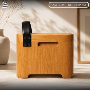 May include: A rectangular light brown wooden storage box with rounded corners and a black leather strap handle attached with four black metal rivets. The box features a horizontal cutout handle on the front face and a smooth, natural wood grain finish.
