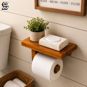 May include: A wall-mounted wooden toilet paper holder with a flat shelf top. The shelf holds a small potted green plant and a rectangular pack of wet wipes. A roll of white toilet paper hangs from the wooden dowel underneath the shelf.