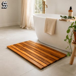 Puede incluir: Una alfombrilla de baño rectangular construida con listones de madera paralelos con un acabado marrón cálido. La alfombrilla presenta un diseño de listones que permite el drenaje, proporcionando una superficie estable al salir de la bañera.