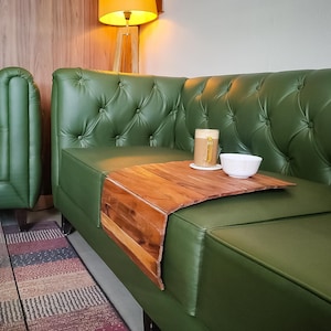 Puede incluir: Un sofá de cuero verde con una bandeja de reposabrazos de madera. Una taza de café y un cuenco blanco pequeño están sobre la bandeja. El sofá tiene respaldo acolchado y está en una habitación bien iluminada.