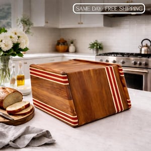 May include: A wooden bread box with a rich brown finish and red and white stripes. The box is rectangular with a slanted front and a hinged top. The kitchen setting includes a loaf of bread and a cutting board.