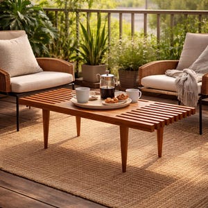 Könnte beinhalten: Ein Holztisch mit Lamellenplatte und abgewinkelten Beinen, auf dem ein Tablett mit Kaffee, Gebäck und zwei weißen Tassen steht. Der Tisch steht auf einem gewebten Teppich, umgeben von Gartenmöbeln und Grün.