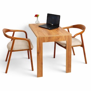 Könnte beinhalten: Ein kleiner Holztisch mit einem Laptop und einer kleinen Vase mit einer roten Rose. Zwei Holzstühle mit beige gepolsterten Sitzen sind auf beiden Seiten des Tisches positioniert. Der Tisch und die Stühle stehen vor einem weißen Hintergrund.
