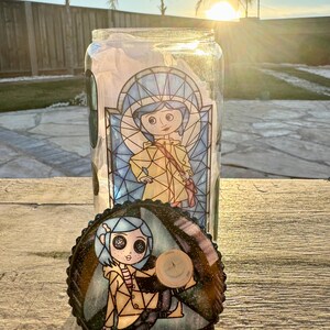 Puede incluir: Un tarro de cristal transparente con una tapa decorativa con un dise&ntilde;o de personaje de dibujos animados. El tarro tiene una ilustraci&oacute;n de estilo vidriera de una ni&ntilde;a con un abrigo amarillo. La tapa tiene un dise&ntilde;o a juego con un bot&oacute;n de madera.