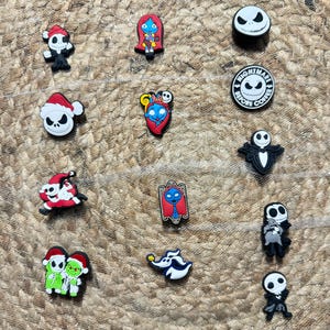 May include: A collection of shoe charms featuring characters from "The Nightmare Before Christmas." The charms include Jack Skellington, Sally, and other characters in various poses and holiday-themed designs. The charms are colorful and made of a rubber-like material.