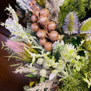 May include: Close-up of a floral arrangement with a mix of textures and colours. It features frosted greenery, pink and white flowers, and bronze glitter berries. The arrangement has a festive and decorative appearance.