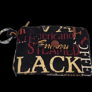 May include: A black fabric zippered pouch with a key ring. The pouch has a flap with a button closure. The fabric has a colorful print with the words "Black" and "Coffee" in large letters.