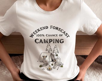 Puede incluir: Camiseta blanca con un gráfico negro que dice "Weekend Forecast 100% Chance of Camping". El gráfico también presenta una ilustración de dibujos animados de dos personas acampando en un bosque.