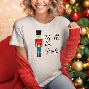 May include: A white t-shirt with a cartoon illustration of a nutcracker soldier and the text "Y'all are Nuts".
