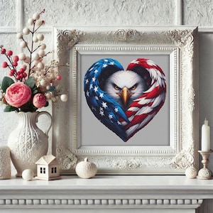 May include: A framed artwork featuring a heart-shaped design with an American flag motif. The heart is formed by the wings of an eagle, with the stars and stripes in blue, white, and red. The artwork is displayed in a white ornate frame.