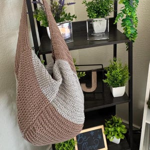 May include: A black metal shelf unit with four shelves. The top shelf has a vintage-style radio with a brown speaker grill and a digital clock display. The second shelf has a brown crocheted bag, a small potted plant with purple flowers, and a clear glass vase with a candle. The third shelf has a small potted plant with green leaves and a silver plaque. The bottom shelf has a small potted plant with green leaves, a wooden sign that says "Be Merry", and a black drawer with a silver knob.