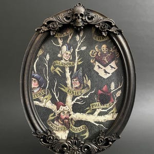 May include: A black oval frame with ornate gold detailing and a skull at the top. Inside the frame is a black and white family tree with the names "Turgis", "Ellaдора", "Sirius", "Phineus", and "Nigellus" written on it.