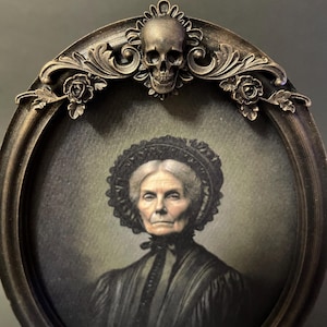 May include: An oval portrait of an elderly woman in a black dress and a lace bonnet, framed in a dark brown ornate frame with a skull and floral accents.