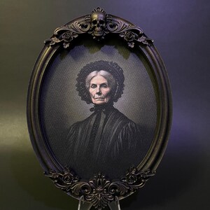 May include: An oval portrait of an older woman in a black dress with a lace collar, framed in a black ornate frame with a skull at the top.