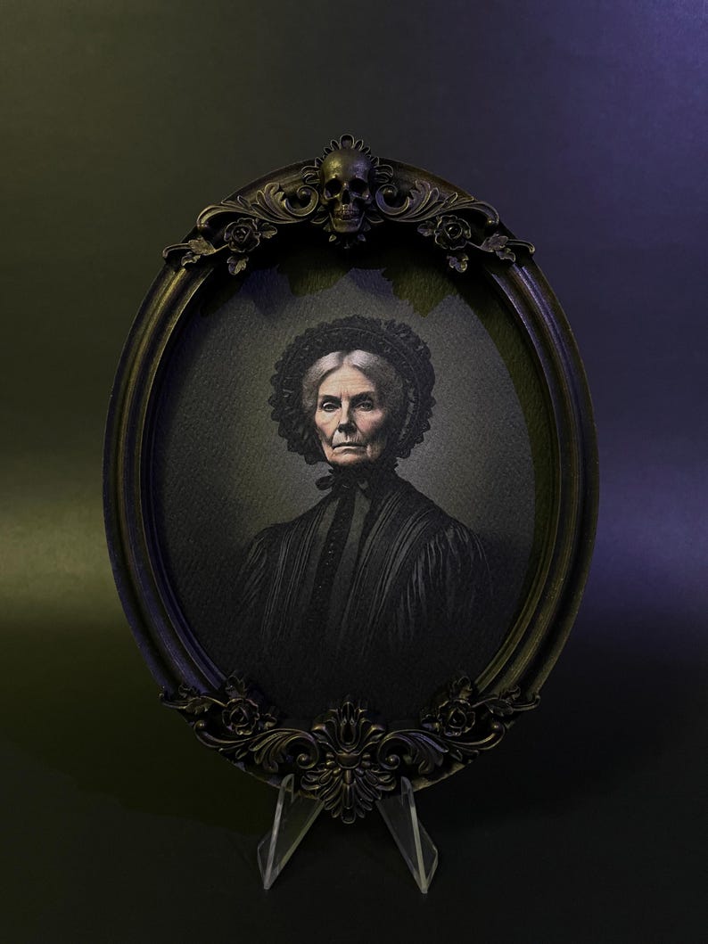 May include: An oval portrait of an older woman in a black dress and a white lace cap. The portrait is framed in a black ornate frame with a skull at the top.
