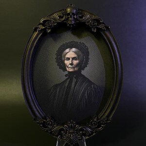 May include: A black oval frame with ornate details, including a skull at the top, holds a black and white portrait of an older woman wearing a black dress and a lace head covering.