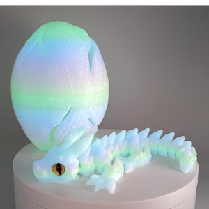 May include: A glowing, pastel-colored dragon emerging from a matching egg. The dragon has a detailed, spiky spine and a focused gaze. The egg is cracked open, revealing the dragon. The overall theme is fantasy and mythical creatures.