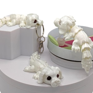 May include: A collection of white, articulated dragon figurines. One dragon is attached to a keychain, another is lying down, and a third is perched on a small, round platform with a green and pink interior.
