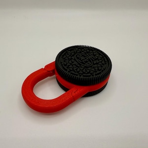 May include: A red plastic carabiner with a black Oreo cookie attached to it.