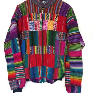 May include: A zip-up jacket featuring a vibrant patchwork design of multicolored striped fabric. The garment includes a high collar, long sleeves with ribbed cuffs, and a central zipper closure, showcasing various woven patterns in red, blue, green, and purple.