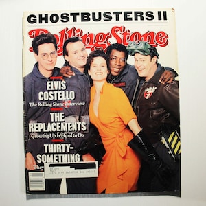 May include: A Rolling Stone magazine cover featuring the cast of Ghostbusters II. The cover features the text "Ghostbusters II" in large, bold letters. The cast members are Elvis Costello, The Replacements, and Thirtysomething. The magazine cover is a red, white, and black color scheme.