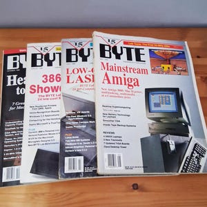 May include: A stack of vintage BYTE magazine issues, featuring covers with headlines like "Mainstream Amiga" and "386 to Show." The magazines showcase computer technology from the late 80s and early 90s, with colorful graphics and text.