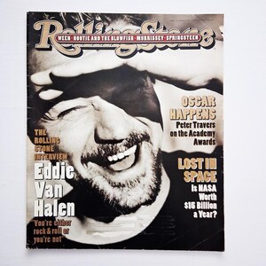 Puede incluir: Portada de la revista Rolling Stone con Eddie Van Halen. La portada incluye el logotipo de Rolling Stone, titulares sobre los Oscar y la pregunta sobre el valor de la NASA. La imagen es en blanco y negro con un retrato sonriente de Eddie Van Halen.