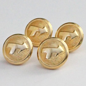 Puede incluir: Cuatro botones dorados con un diseño circular y un símbolo de flecha en relieve. Los botones tienen una textura acanalada alrededor de los bordes y un acabado brillante. La flecha es de un color dorado más claro.