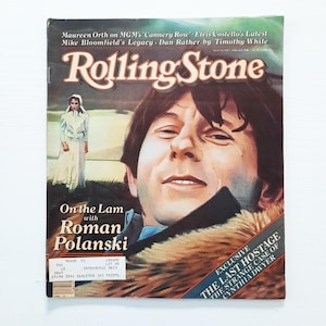 Pode incluir: Uma capa de revista Rolling Stone vintage com um retrato de um homem com cabelo castanho e um casaco forrado a pele. O título da revista está em letras grandes e estilizadas. O texto adicional inclui o nome "Roman Polanski" e o título "The Last Hostage."