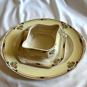Puede incluir: Un juego de servir de cerámica amarilla vintage con adornos florales y dorados. El juego incluye una fuente ovalada grande, un plato cuadrado y una salsera pequeña. El diseño floral presenta flores rojas, azules y amarillas.