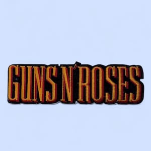 May include: Embroidered patch featuring the text "GUNS N ROSES" in a bold, stylized font. The letters are in a gradient of gold and red, outlined in black. The patch is rectangular and has a black border.