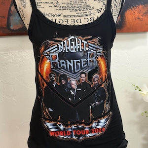 Puede incluir: Camiseta sin mangas negra con la banda Night Ranger. La camiseta tiene un diseño gráfico de los miembros de la banda con las palabras "NIGHT RANGER" y "WORLD TOUR 2024" en un diseño estilizado. La camiseta sin mangas tiene tirantes finos.