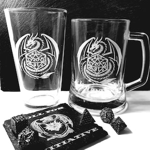May include: A clear glass pint glass and a clear glass beer mug, both etched with a dragon coiled around a twenty-sided die. A square black slate coaster features a dragon head emblem and the text ROLL FOR INITIATIVE, with four metal dice.