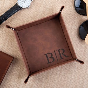 Può includere: Un vassoio valet in pelle marrone con un design monogrammato. Le iniziali "B/R" sono incise al centro del vassoio.