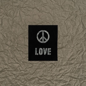 May include: A black square with the word "LOVE" in white, block letters and a white peace symbol. The background is a textured, crumpled, tan paper.