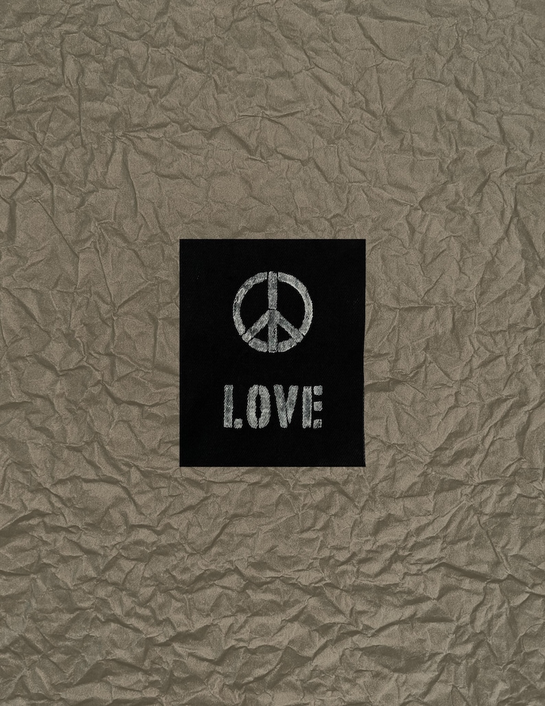 May include: A black square with the word "LOVE" in white, block letters and a white peace symbol. The background is a textured, crumpled, tan paper.