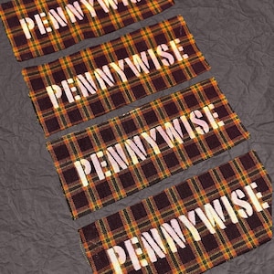May include: Four rectangular patches with a plaid pattern in shades of brown, yellow, and green. The word "PENNYWISE" is printed in white across each patch. The patches are arranged diagonally on a textured gray surface.