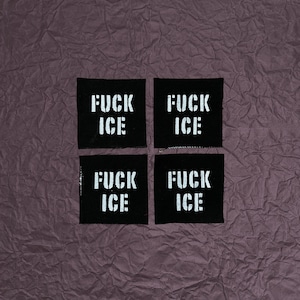 May include: Four black fabric patches with the words "FUCK ICE" in bold, white, stencil-style lettering. The patches are arranged in a square on a textured, dark purple background.