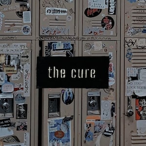 May include: A collage of beige lockers covered in stickers and graffiti. A black rectangle in the center displays the text "the cure" in white, stylized lettering. The lockers have various locks and are decorated with posters and stickers.