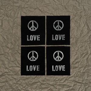 May include: Four black square patches with a white peace symbol and the word "LOVE" printed in a distressed font. The patches are arranged in a 2x2 grid on a textured, brown surface.