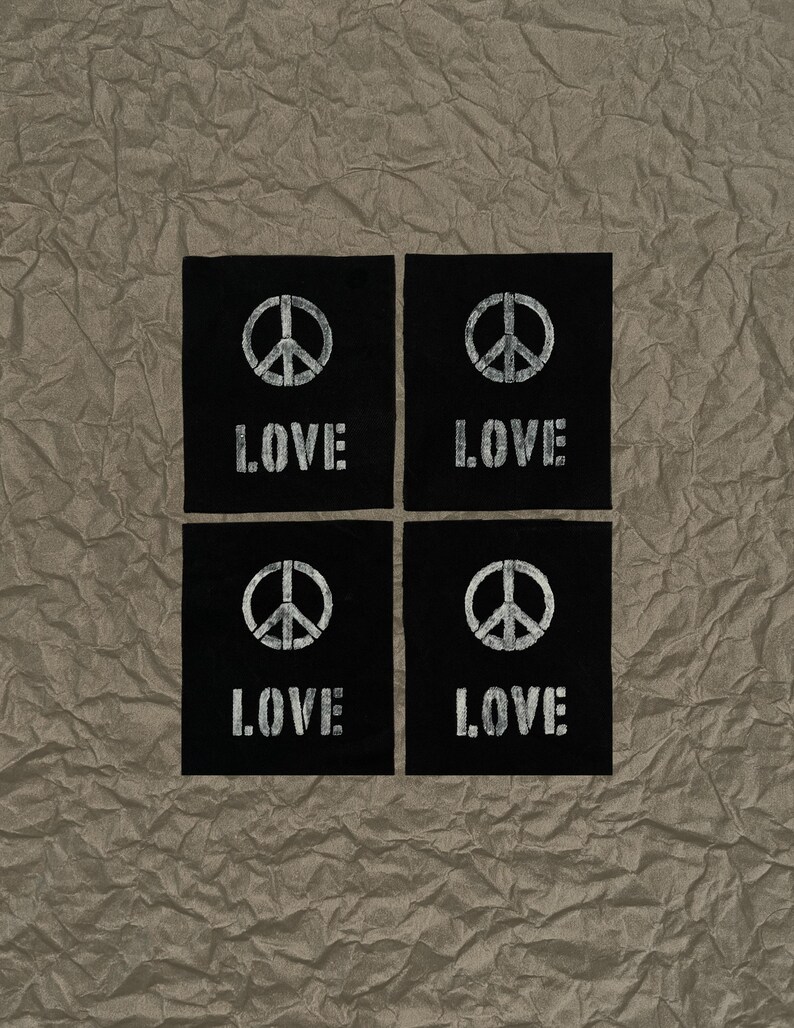 May include: Four black square patches with a white peace symbol and the word "LOVE" printed in a distressed font. The patches are arranged in a 2x2 grid on a textured, brown surface.