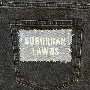 May include: A black pair of jeans with a back pocket that has a blue patch sewn on it. The patch has white text that says "SUBURBAN LAWNS".