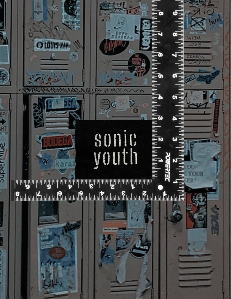 May include: A black square patch with the text "sonic youth" in white lettering is placed over a ruler. The background features a series of lockers covered in stickers and graffiti, creating a vintage aesthetic.
