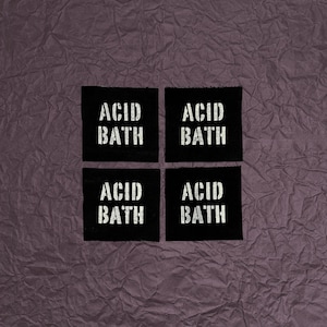 May include: Four black square patches with the words "ACID BATH" printed in white, arranged in a 2x2 grid. The background is a textured, crumpled, dark purple surface.