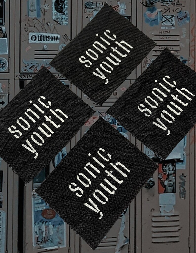 May include: Four black fabric patches with the white text "sonic youth" arranged in a diamond pattern. The background is a locker door covered in graffiti and stickers.