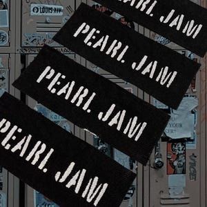 May include: Four rectangular black fabric patches arranged diagonally, each featuring the text PEARL JAM embroidered in white thread. The patches have a woven texture and clean, straight edges, displaying the band name in a bold, sans-serif font.