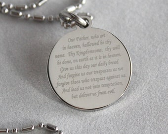 May include: A silver necklace with a round pendant featuring the Lord's Prayer engraved on it. The pendant is attached to a silver chain.