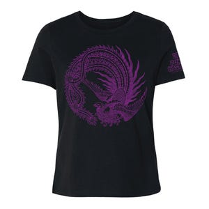 K&ouml;nnte beinhalten: Ein schwarzes Kurzarm-T-Shirt mit einer kreisf&ouml;rmigen violetten Grafik eines Ph&ouml;nix mit detaillierter Federzeichnung. Auf dem rechten &Auml;rmel befindet sich der violette Schriftzug "THE PUNK HASTA". Das T-Shirt hat einen Rundhalsausschnitt.