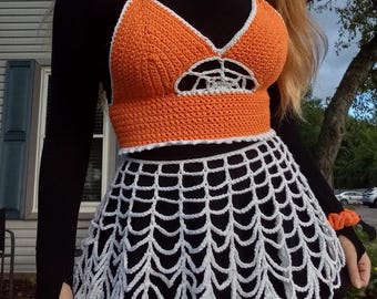 May include: A crocheted orange halter top with white trim and a spiderweb cutout design, paired with a white crocheted skirt that resembles a spiderweb.